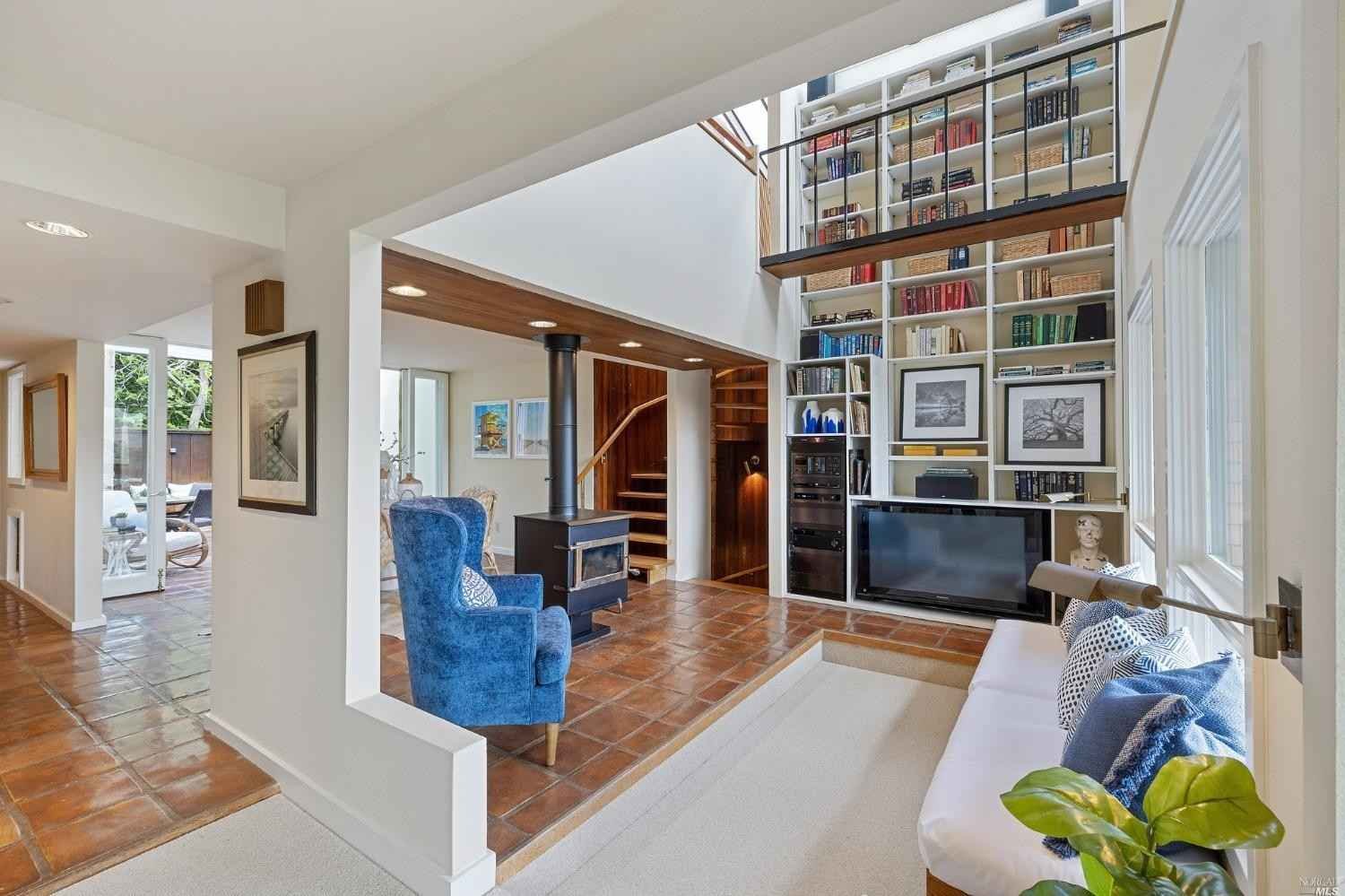 Living room with a built-in white bookshelf, a black TV, blue armchair, white sofa with blue pillows, and a wood-burning stove on a raised brick platform.