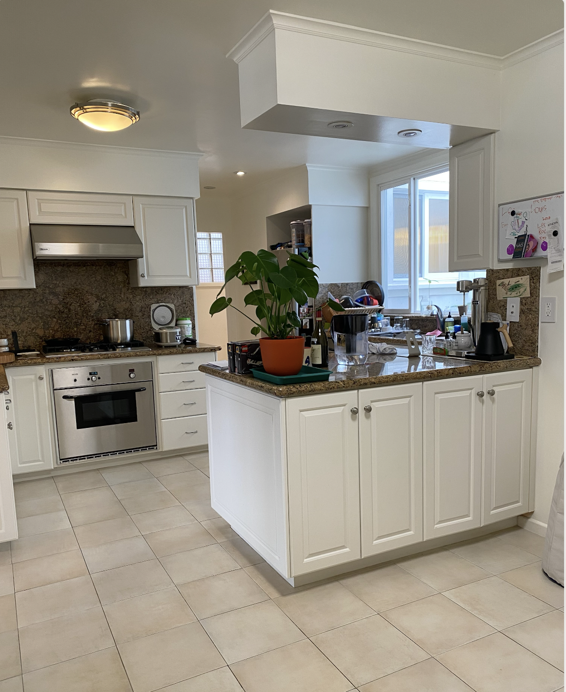 Kitchen with white cabinets, granite countertops, a potted plant on the island, and various kitchen appliances and utensils.