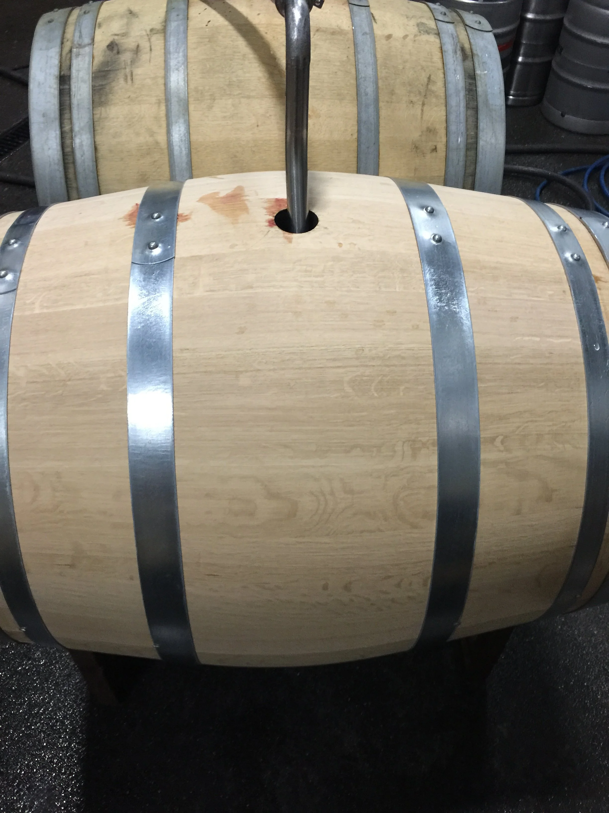 A wooden barrel with metal hoops on a black surface, used for aging or storing liquids, with a metal tap or spigot on top.