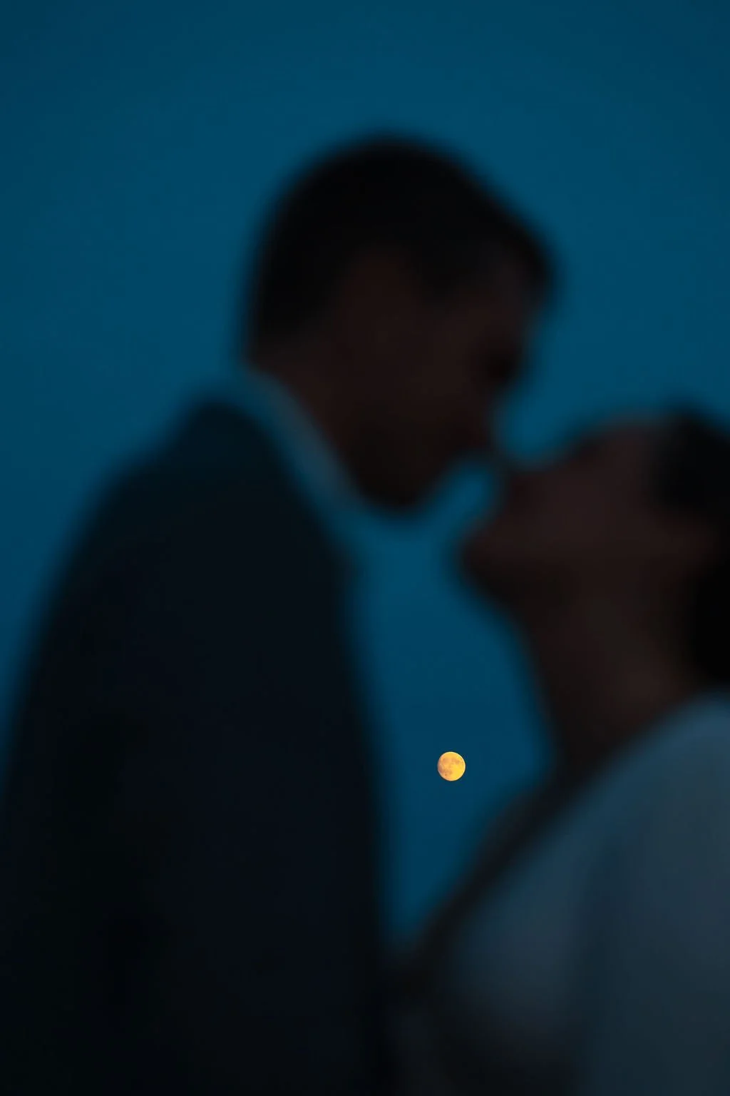 A blurry image of two people in close proximity, with a visible moon in the background during nighttime.