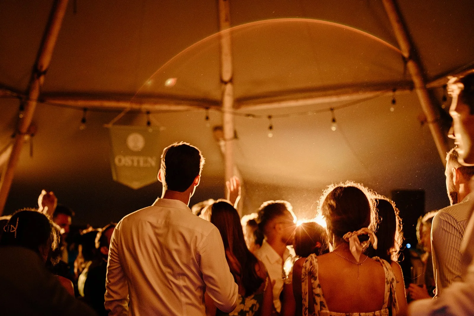 People dancing and socializing under a large tent at night, with warm lighting and a 'Catering' sign visible in the background.