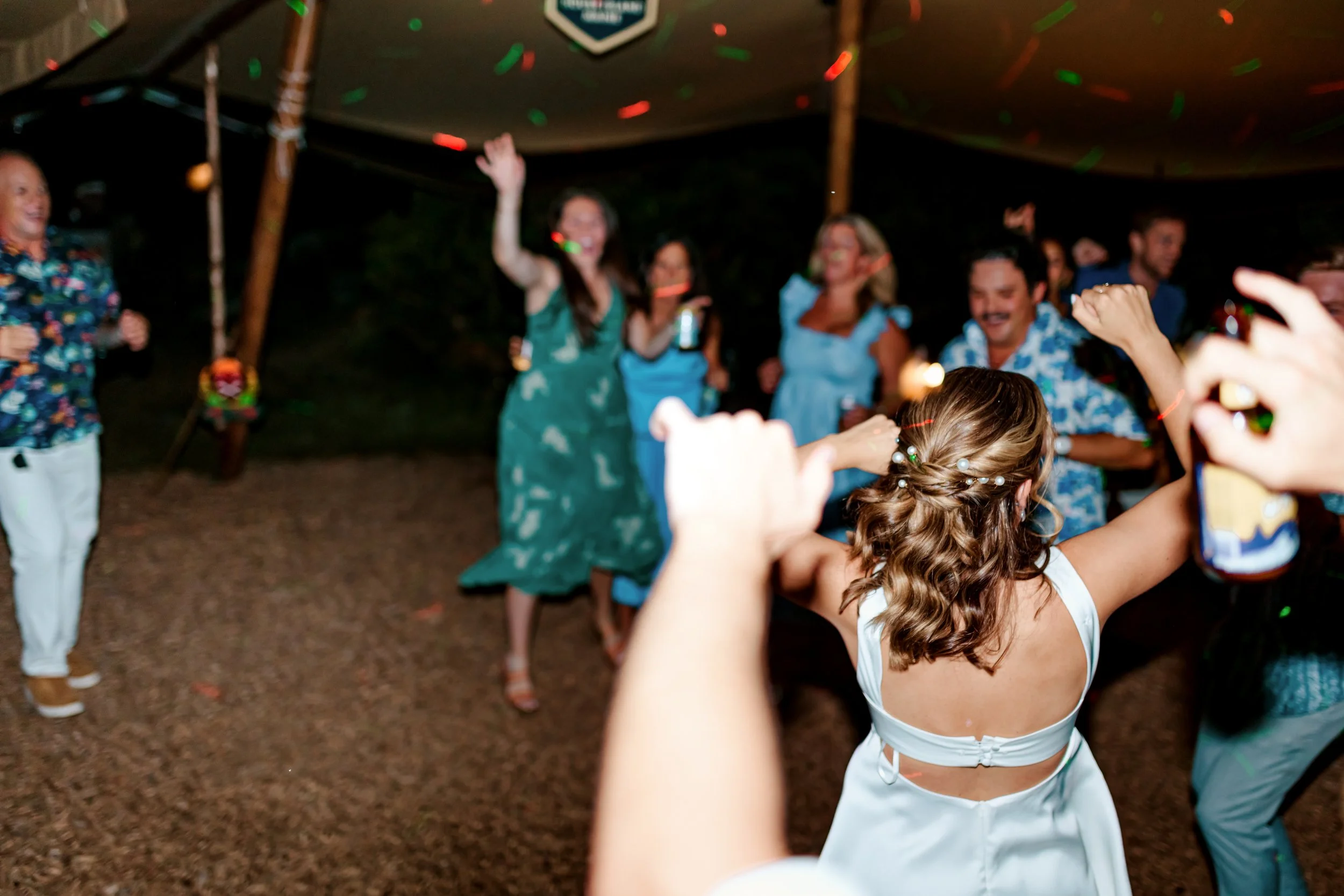 People dancing and celebrating at a party under a tent at night, with colorful confetti falling.