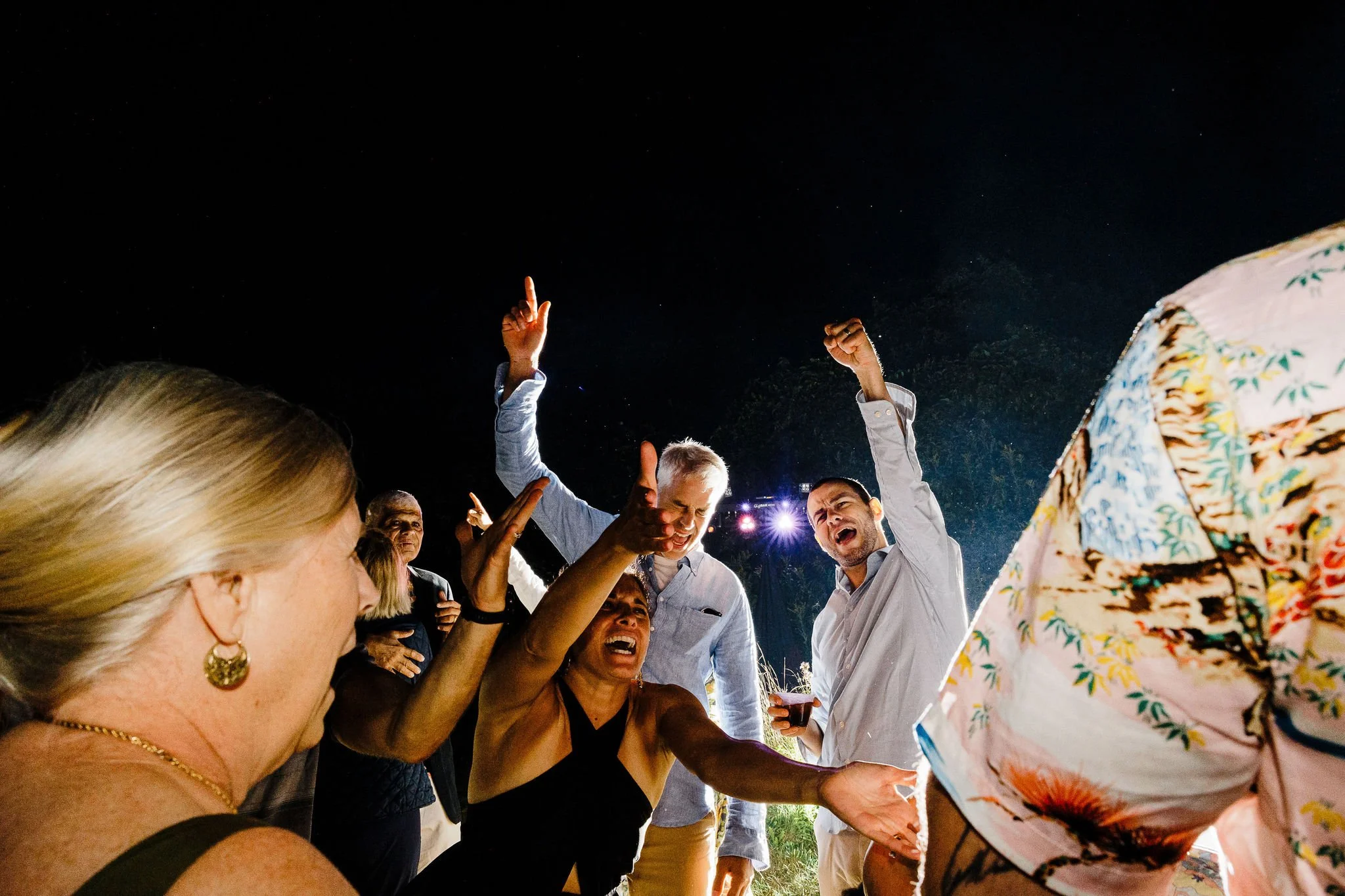 People celebrating and dancing at an outdoor party at night, some with raised arms and joyful expressions.