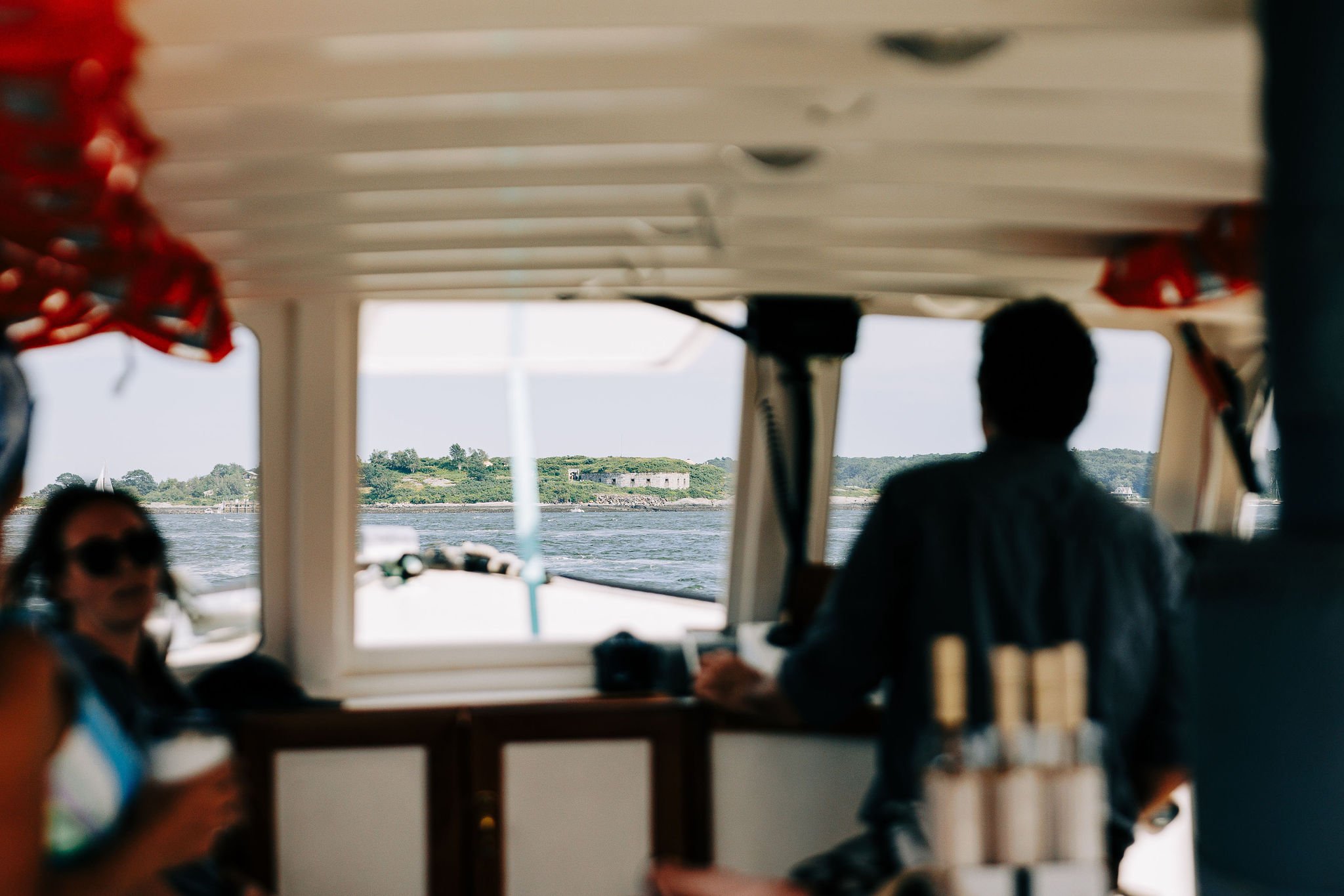 Passengers sitting inside a boat with a view of the water and land through the windows.