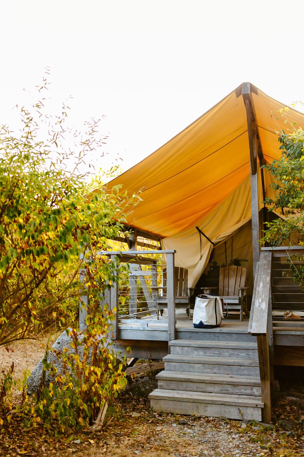 A wooden deck with Adirondack chairs under a yellow canopy, surrounded by green foliage.