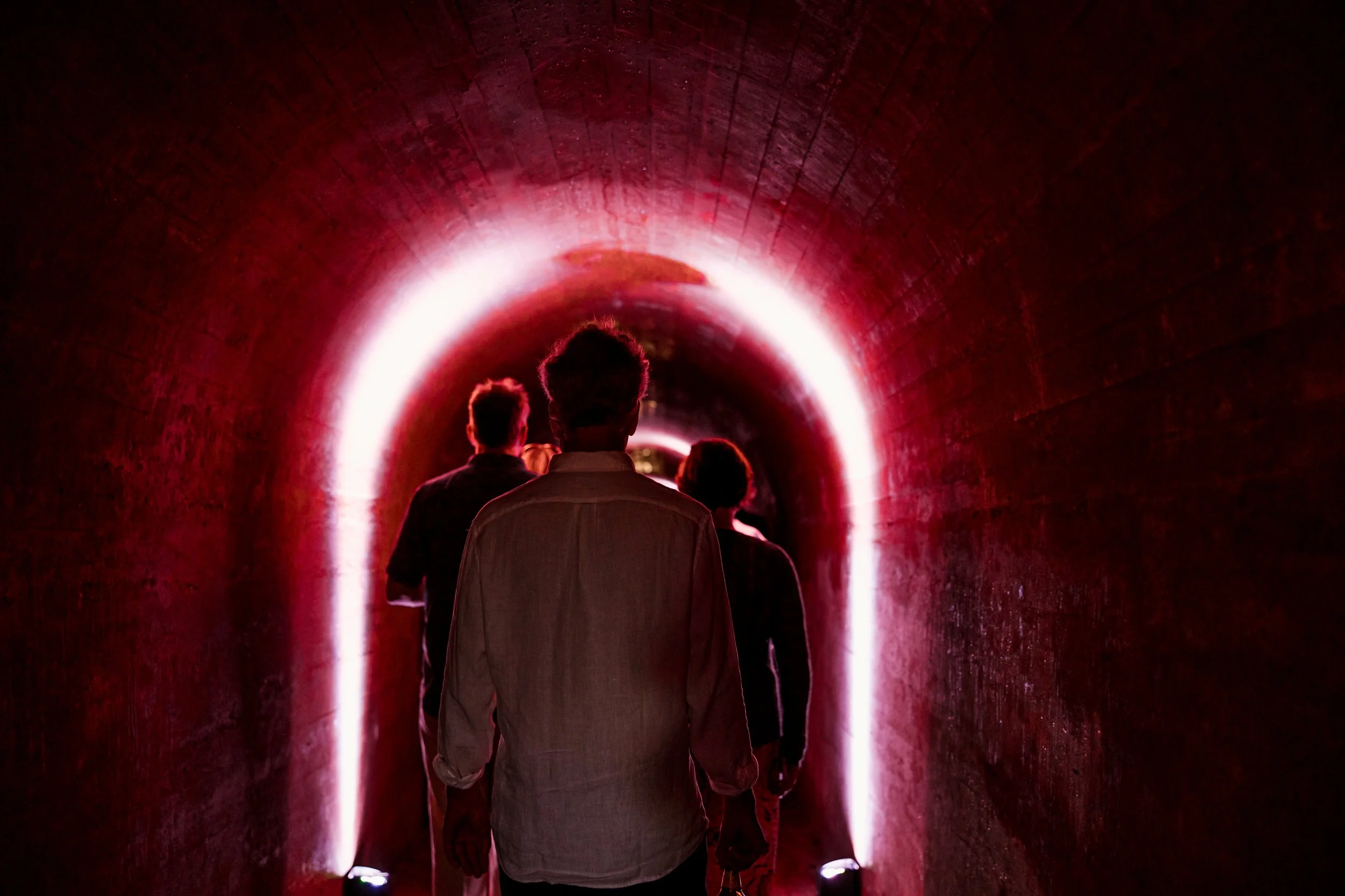 People walking through a tunnel illuminated with bright pink and white neon lights.