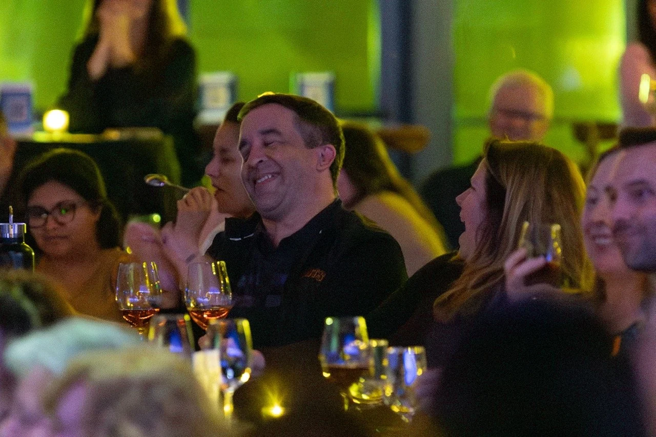 People laughing and enjoying themselves at a social event with wine glasses on the table.