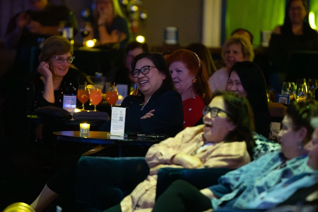 People sitting at tables enjoying a comedy or entertainment show in a dimly lit venue.