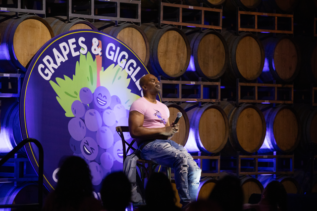 Comedian on stage at Grapes & Giggles comedy event with barrels in background.