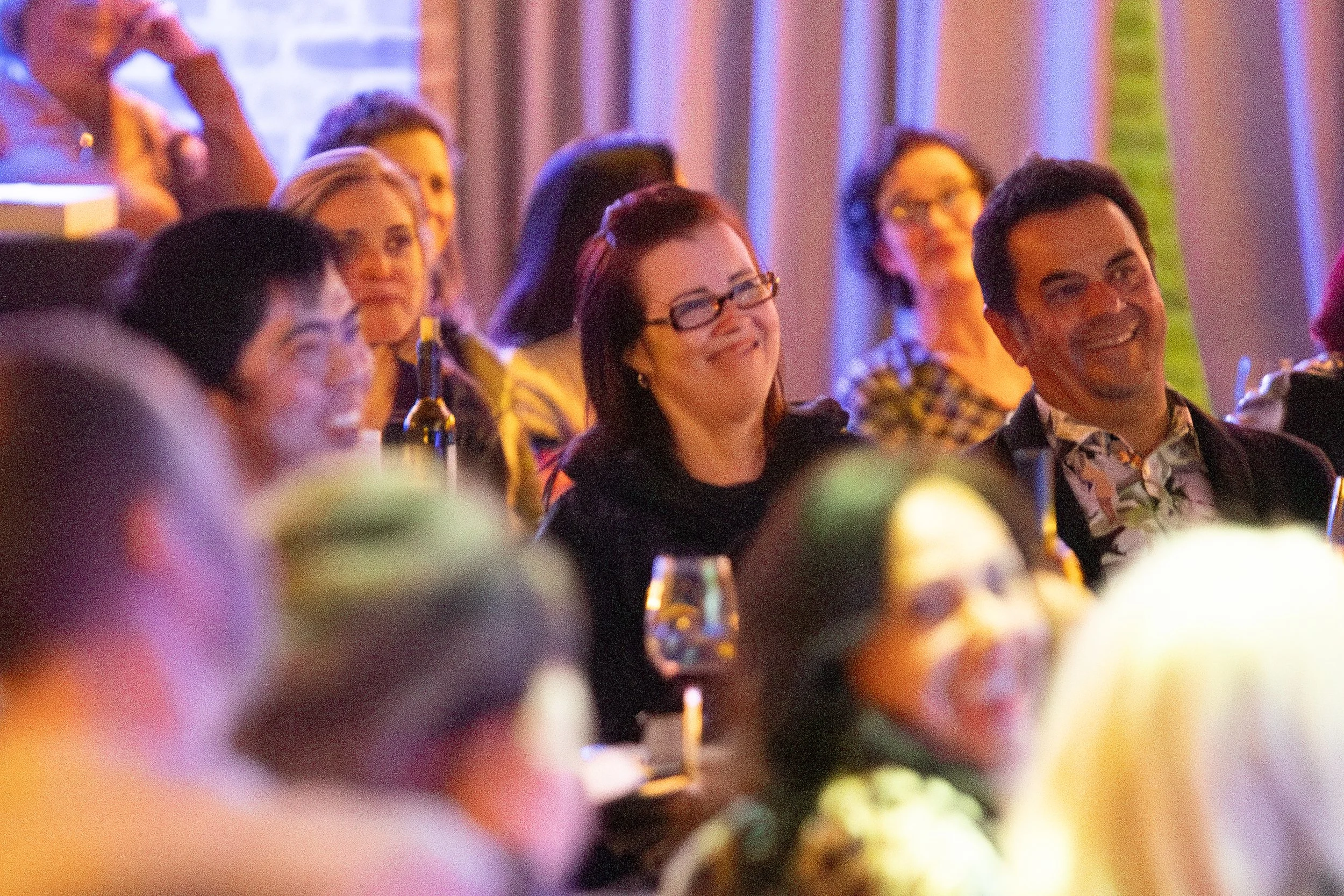 Smiling people seated at an event with wine glasses