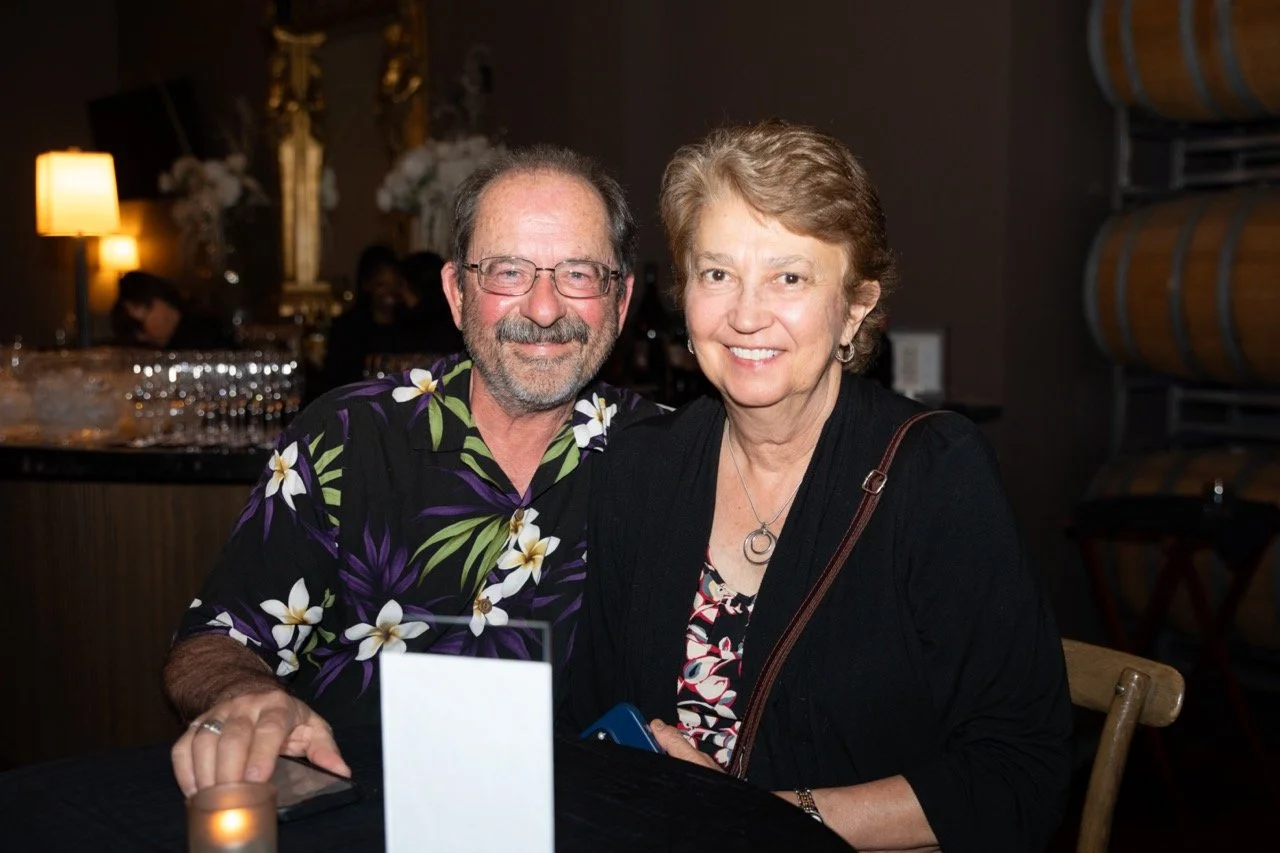 A smiling couple sitting at a table in a dimly lit restaurant with wine barrels in the background.