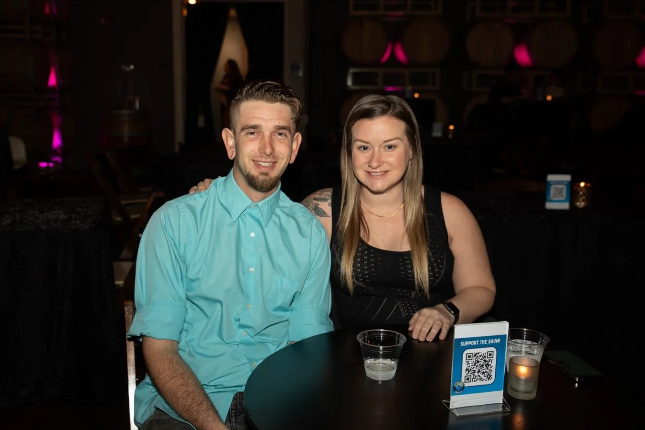 Man and woman sitting at a table in a dimly lit venue with candles and QR code sign.