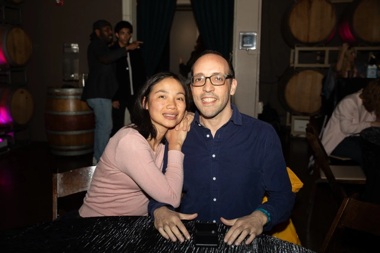 A couple posing for a photo at a party with wine barrels in the background.