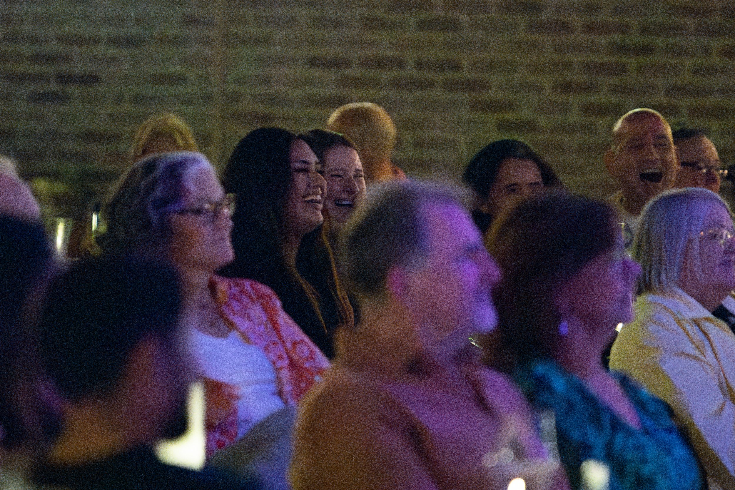 Audience members laughing during an event in a dimly lit venue with brick walls.