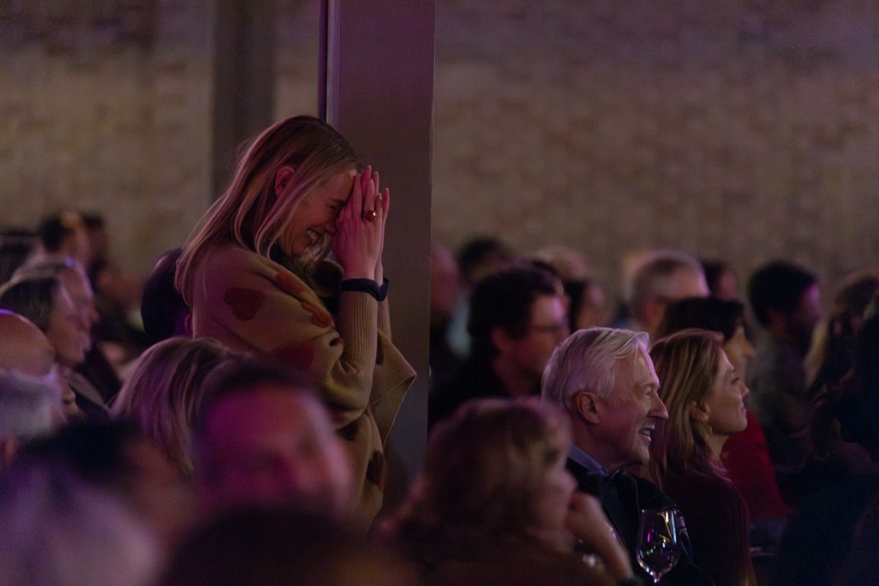 Audience enjoying a performance, with focus on a smiling woman in the foreground.