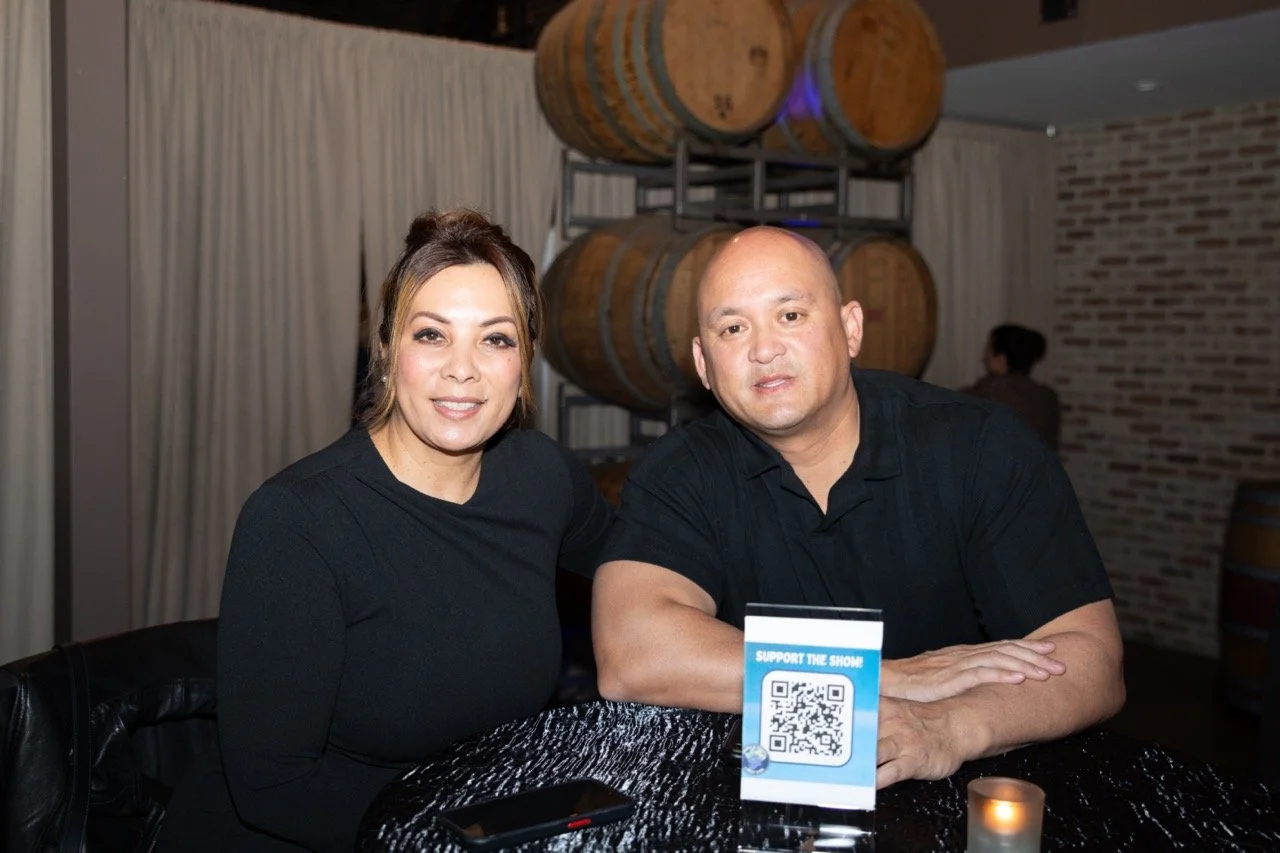 Two people posing at a table with QR code sign in a dimly lit venue with wine barrels and brick wall.
