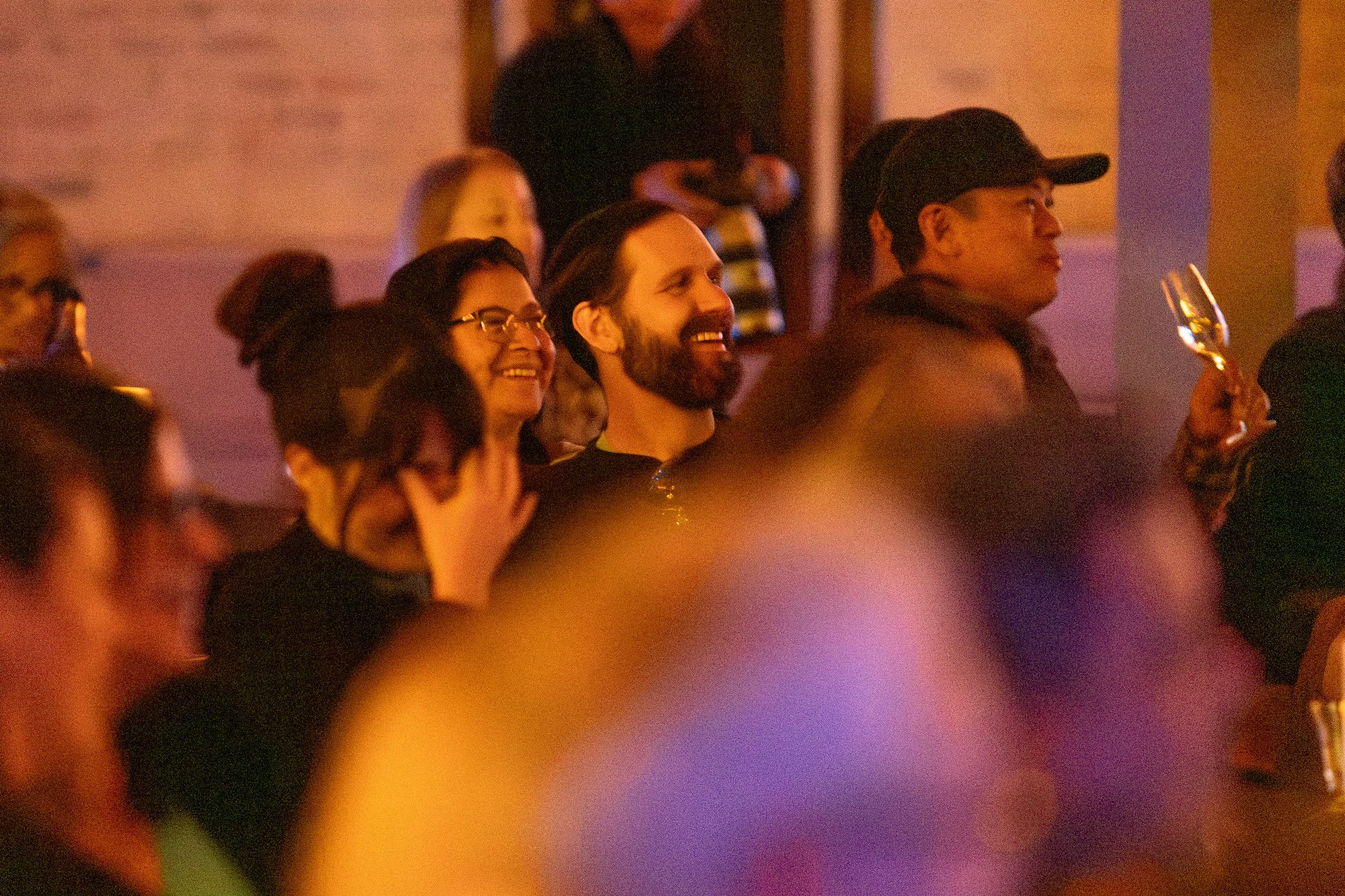 People sitting together at an event, smiling and holding glasses.