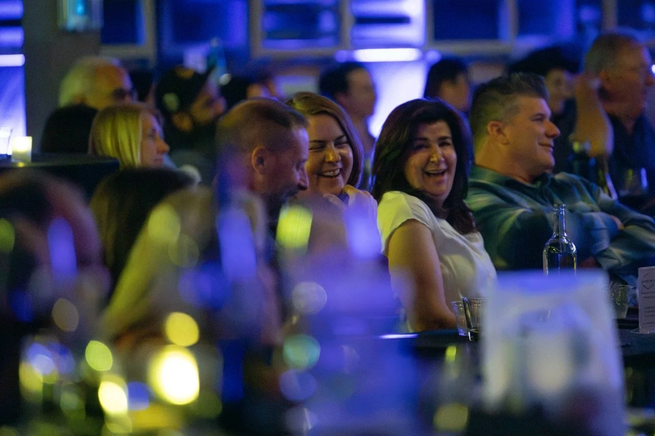 Audience laughing at a comedy club with blue lighting.