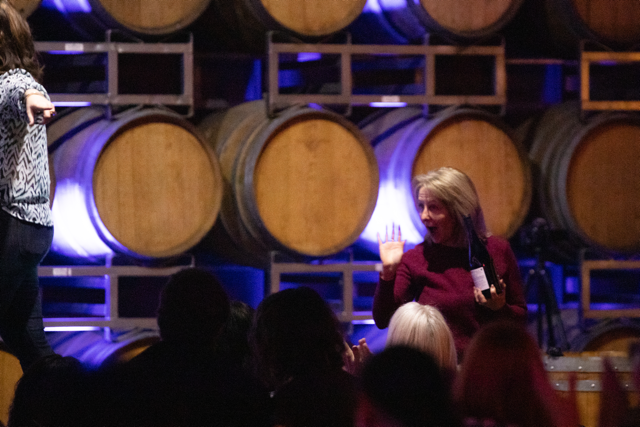 Women engaging in conversation at a wine cellar event with barrels in the background.
