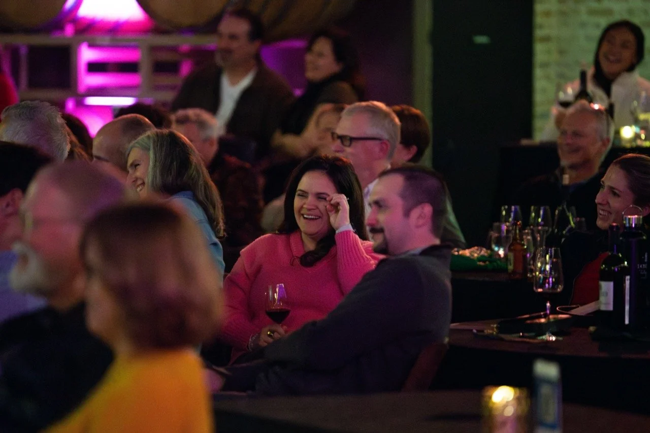Audience laughing and enjoying a live event in a dimly lit venue.