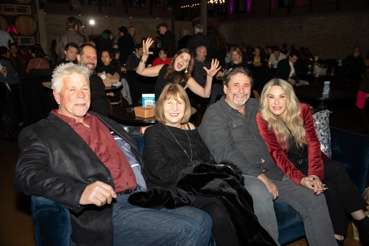 Group of people sitting and smiling in a lively indoor party setting.