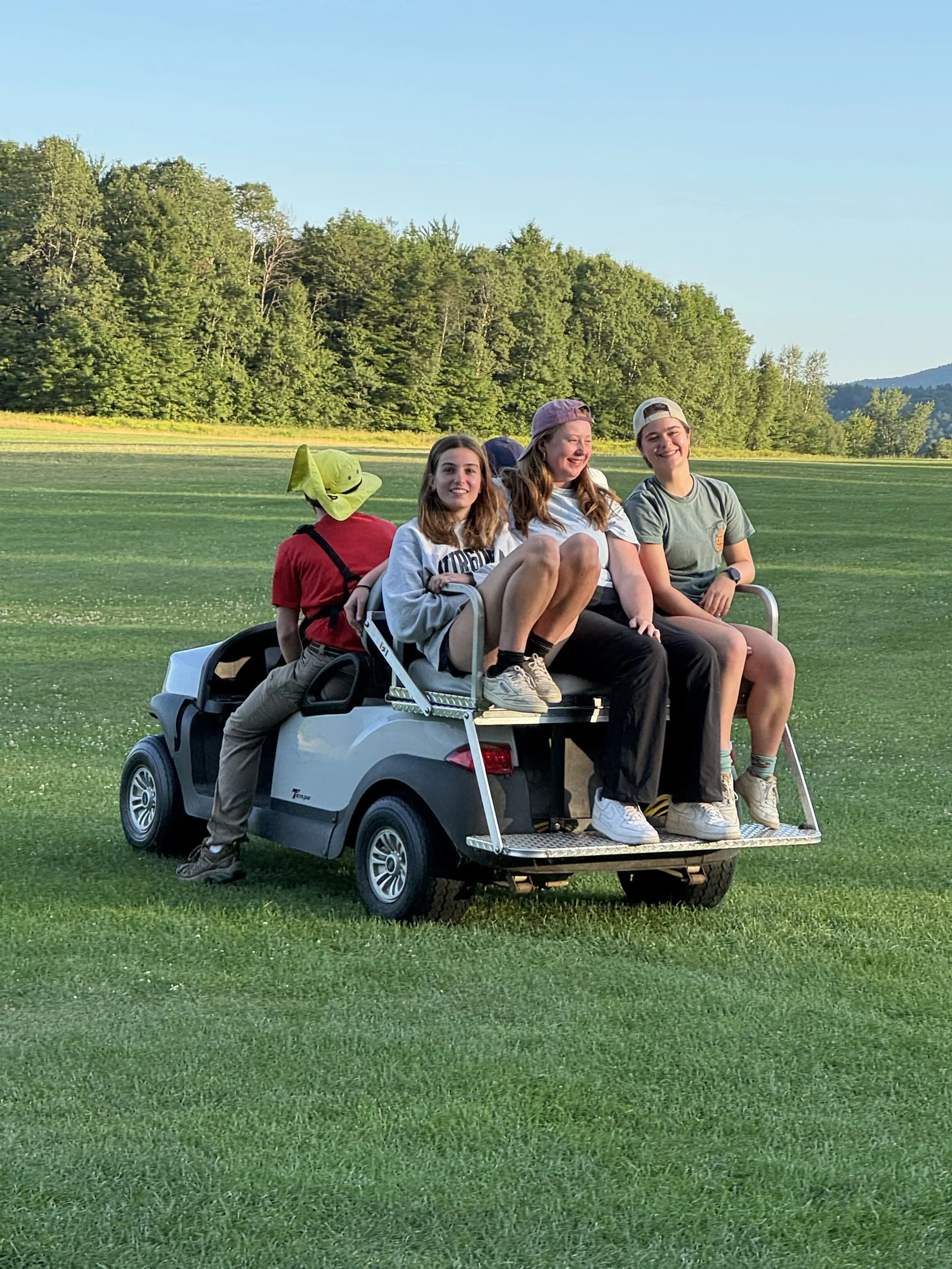 Close-up of a smiling woman with curly hair, wearing glasses, hoop earrings, layered necklaces, and a striped shirt.