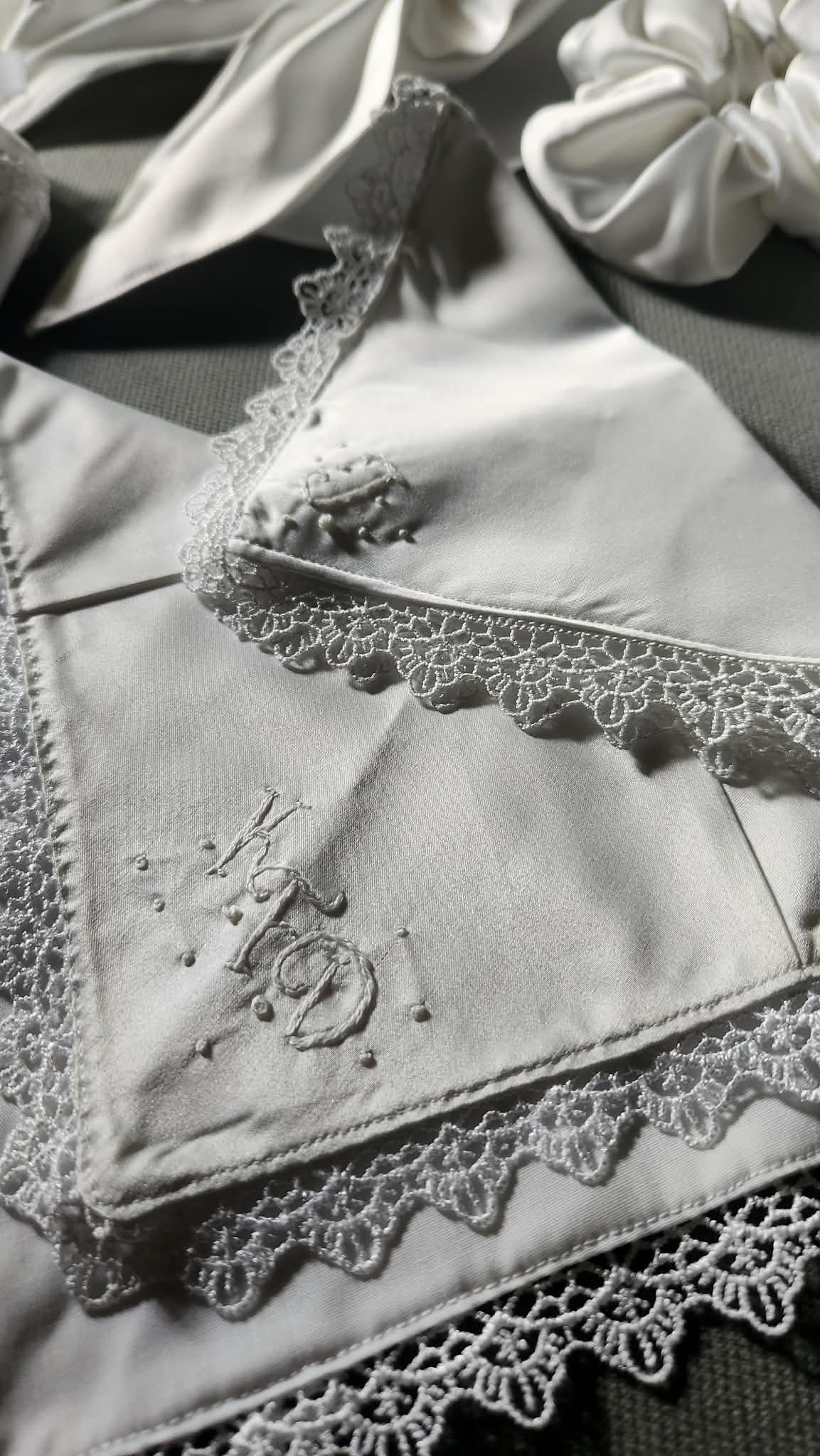Close-up of a white satin pillow with embroidered text and lace trim, surrounded by folded white fabric and accessories.
