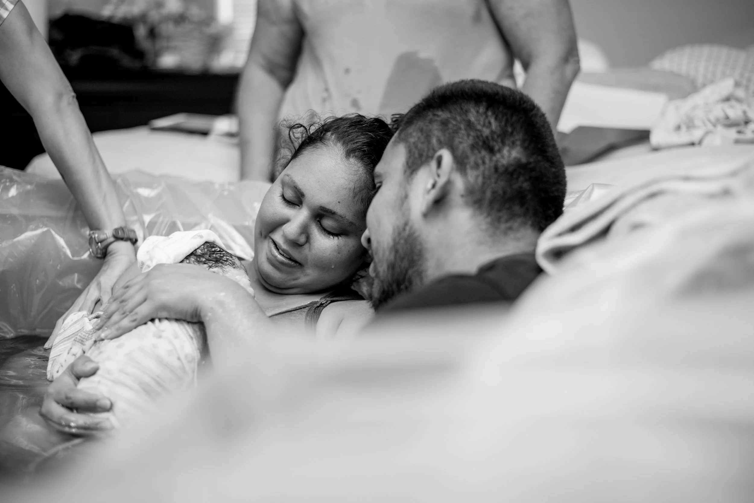 A woman giving birth to a baby in a hospital, surrounded by her partner and medical staff, in a black and white photo.