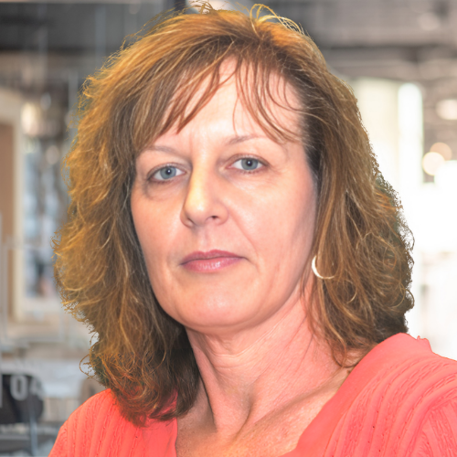 Portrait of a woman with light brown hair wearing a coral shirt in an office setting.