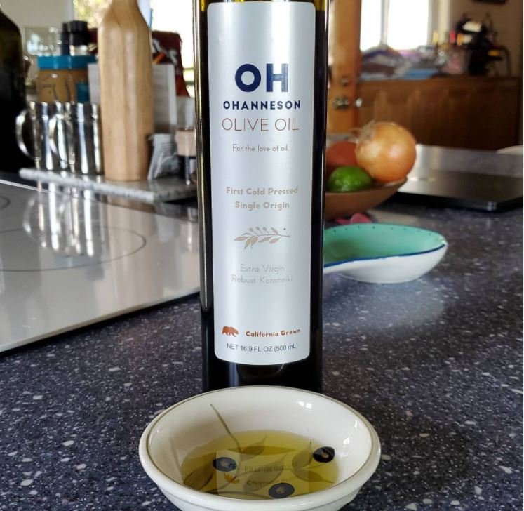 A bottle of OH Olive oil, sat behind a dish filled with oil.
