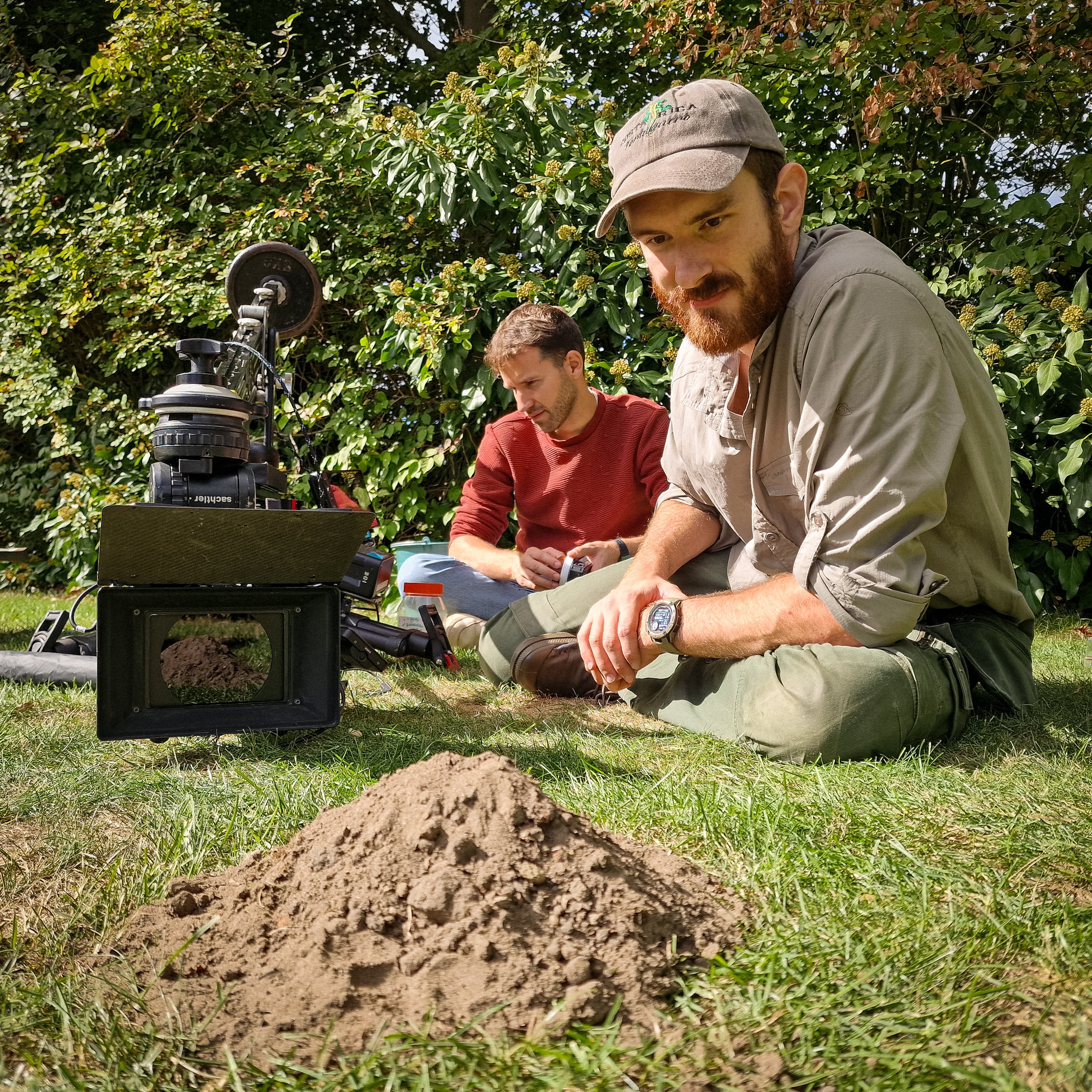 Twee mannen in het gras op een dag, met een scherm en camera's, die wachten op het tevoorschijnkomen van een jonge mol.