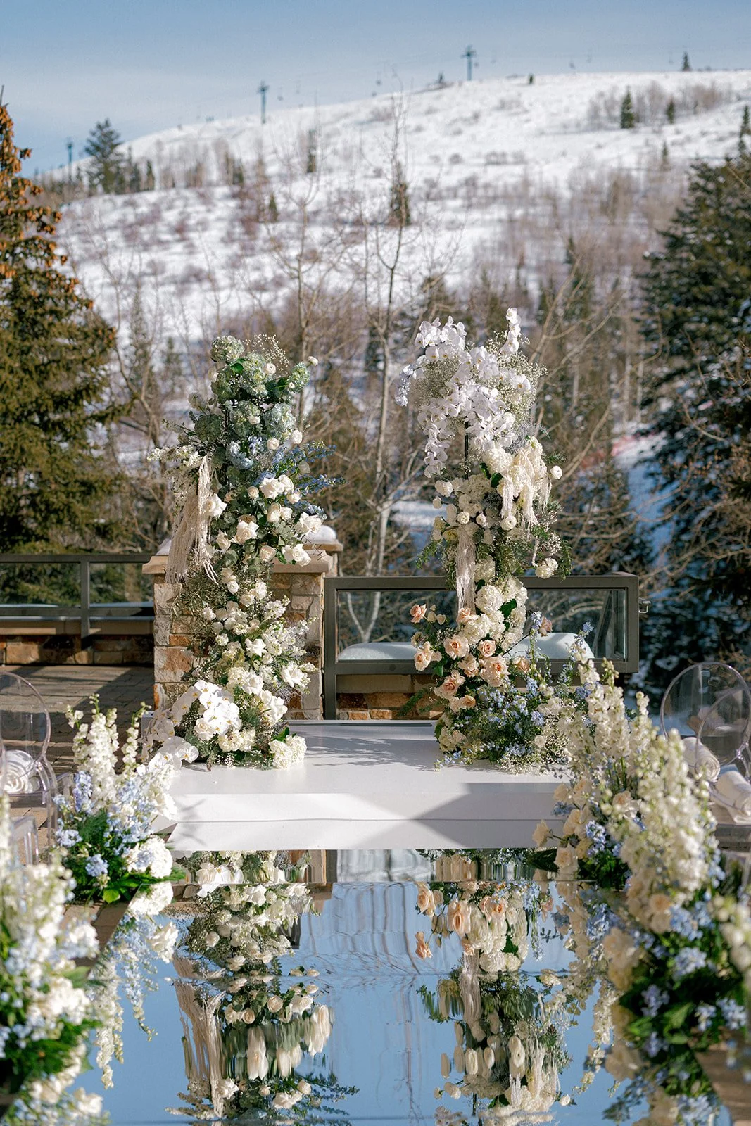  Winter wedding ceremony floral installation at St. Regis Deer Valley featuring white roses, tinted gray orchids, and snowy mountain backdrop. 