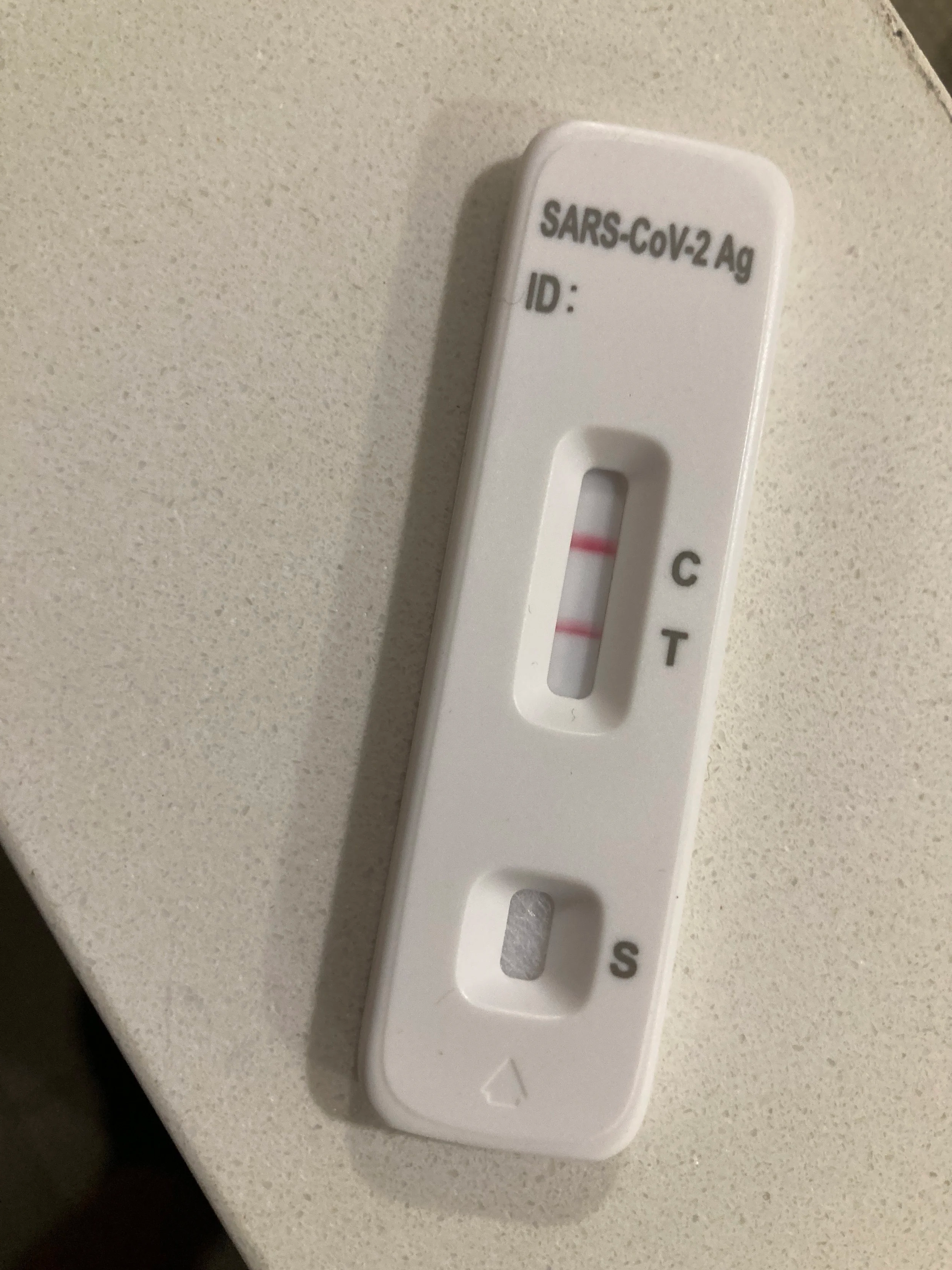 A Covid rapid test with two red lines, marking one for the control and one for the test signifying a positive result lies on a white countertop.