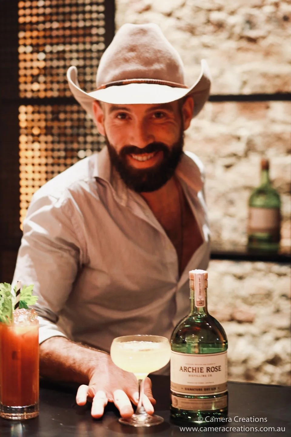 Whisky Pete smiling behind the bar, cowboy hat on, ready to pour and perform.