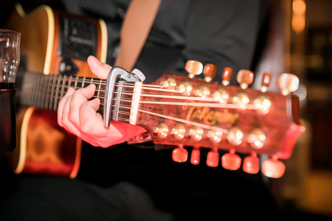 Person playing an acoustic guitar with a capo on the neck, in a cozy indoor setting.