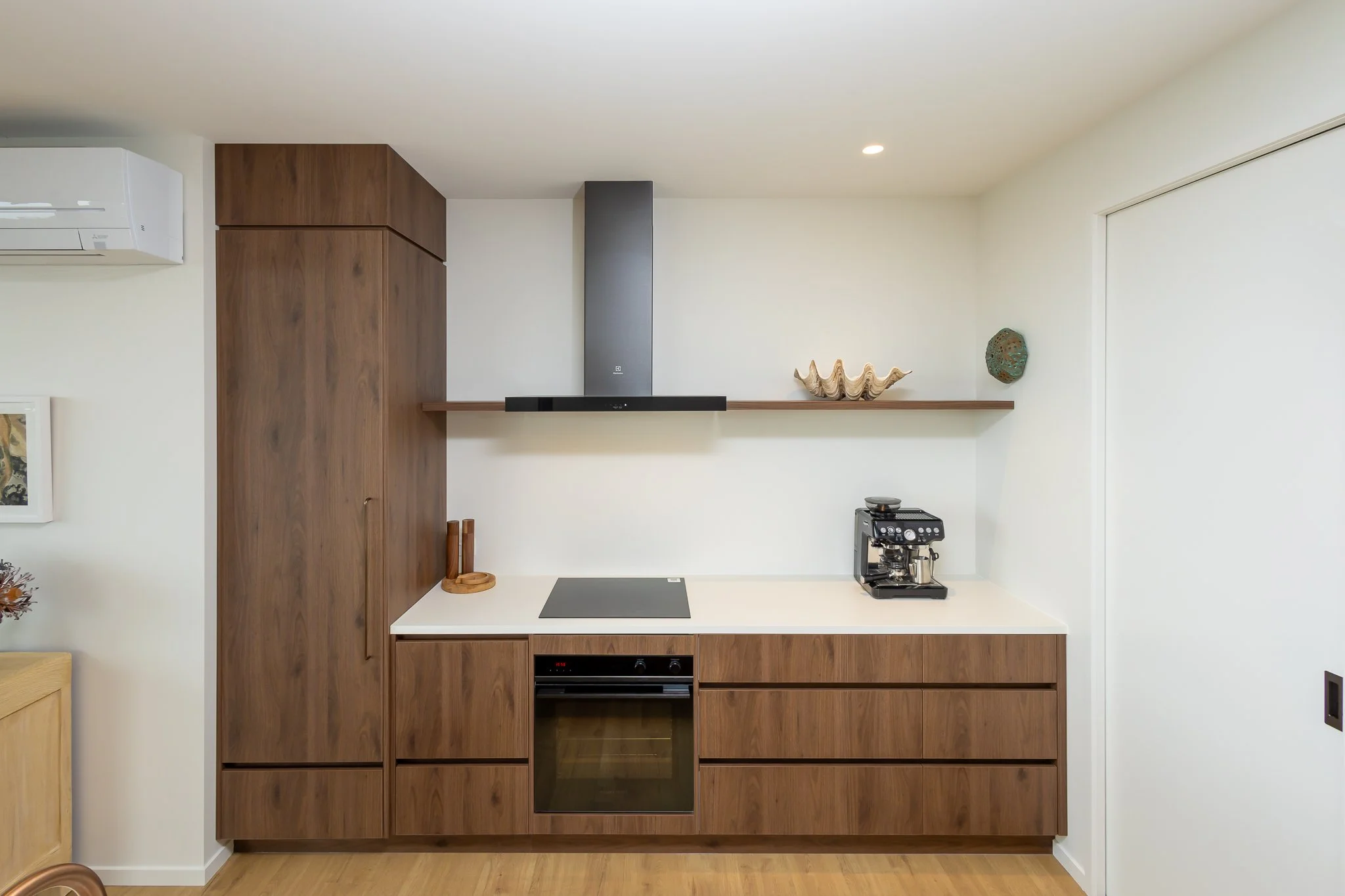 Modern kitchen interior photography with white walls, wooden cabinets, black oven, coffee machine, and decorative objects on a shelf.