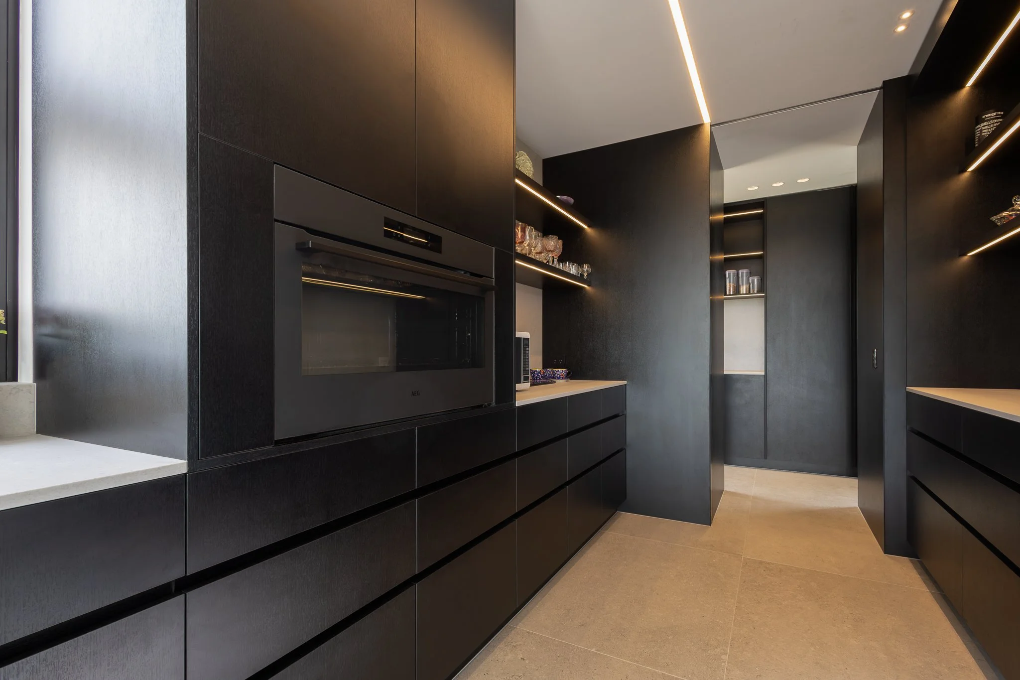 Modern kitchen interior photography with black cabinets, built-in oven, open shelves with glasses and dishes, and sleek lighting fixtures.