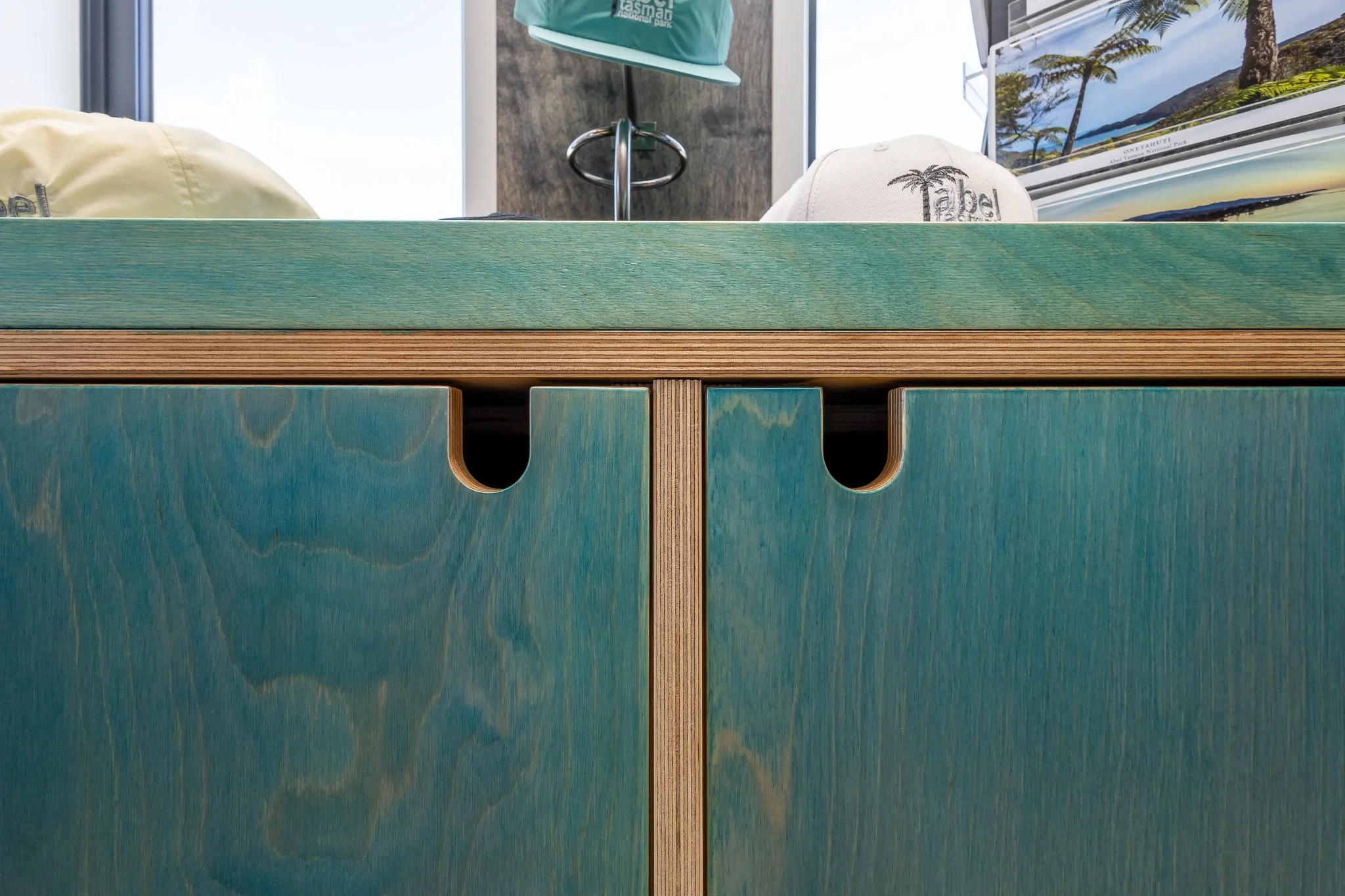 Close-up of wooden furniture with blue and natural wood finish, with hats and a map or brochure with scenic landscape in the background.