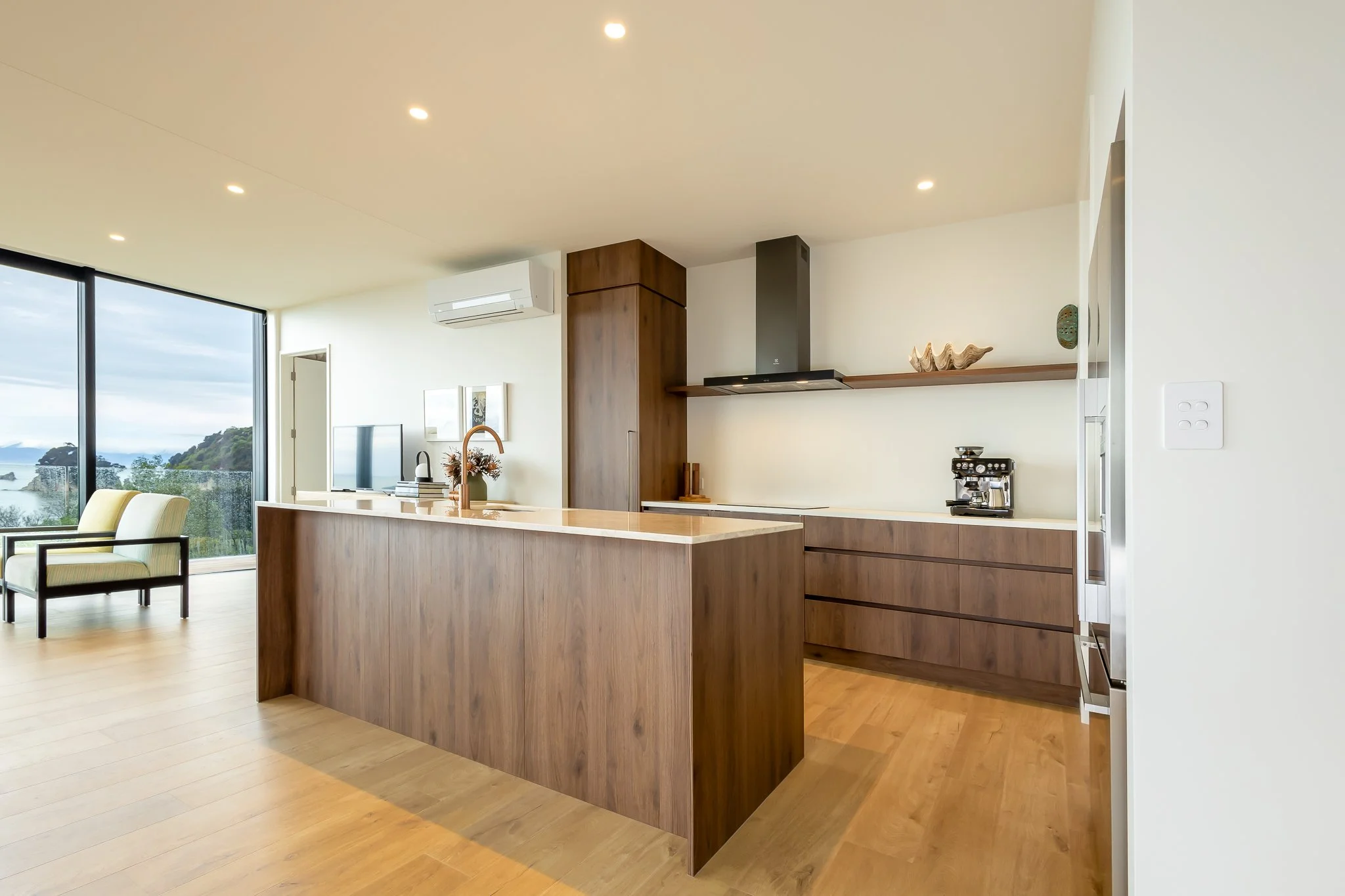 Modern open-concept kitchen interior photography with wooden cabinets, a kitchen island, and a view of the ocean through large windows.