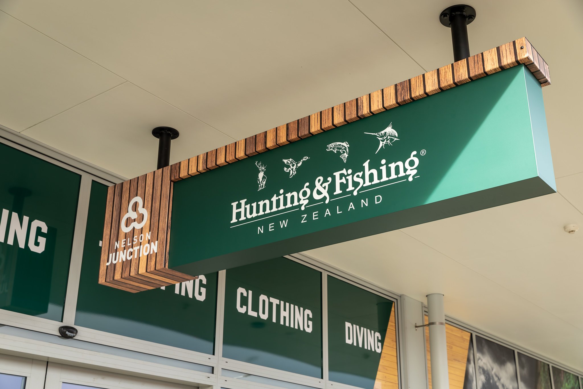 Storefront sign for Hunting & Fishing New Zealand, Nelson Junction, featuring fish illustrations and a decorative wooden frame.