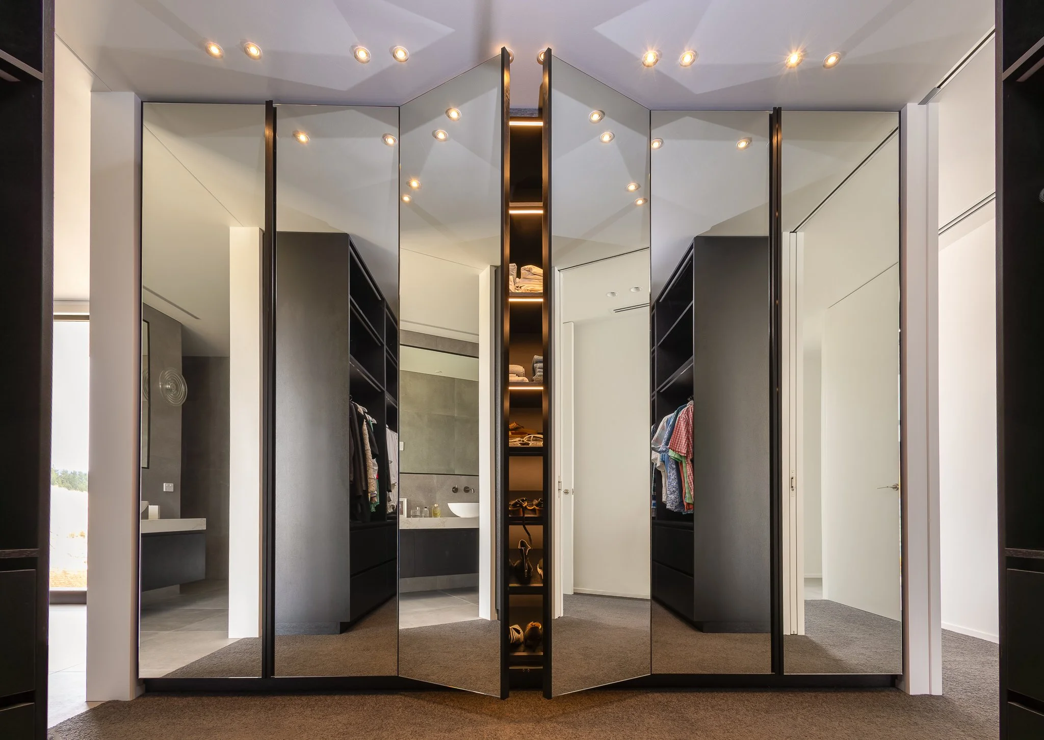 Modern walk-in closet interior photography with black shelving and doors, mirrored sliding doors, and interior lighting displaying clothes and shoes.