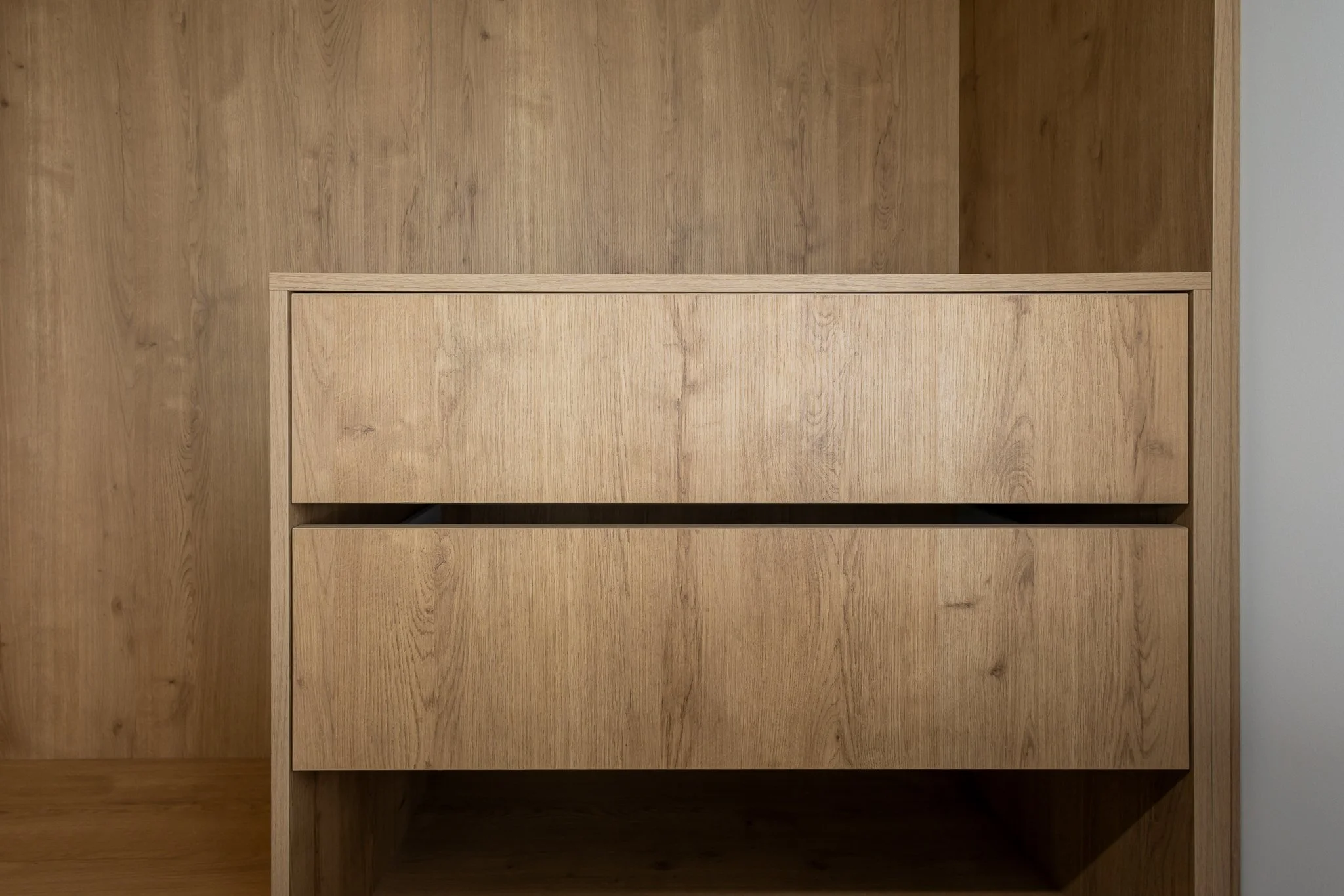 A wooden cabinet interior photography with open shelves, made of light-colored wood, against a matching wood-paneled wall.