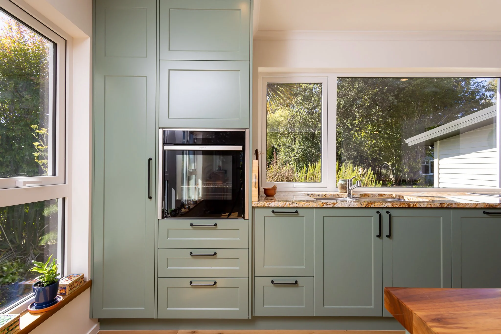 Kitchen with green cabinets, a granite countertop, large windows showing greenery outside, a potted plant on the windowsill, and a built-in oven.