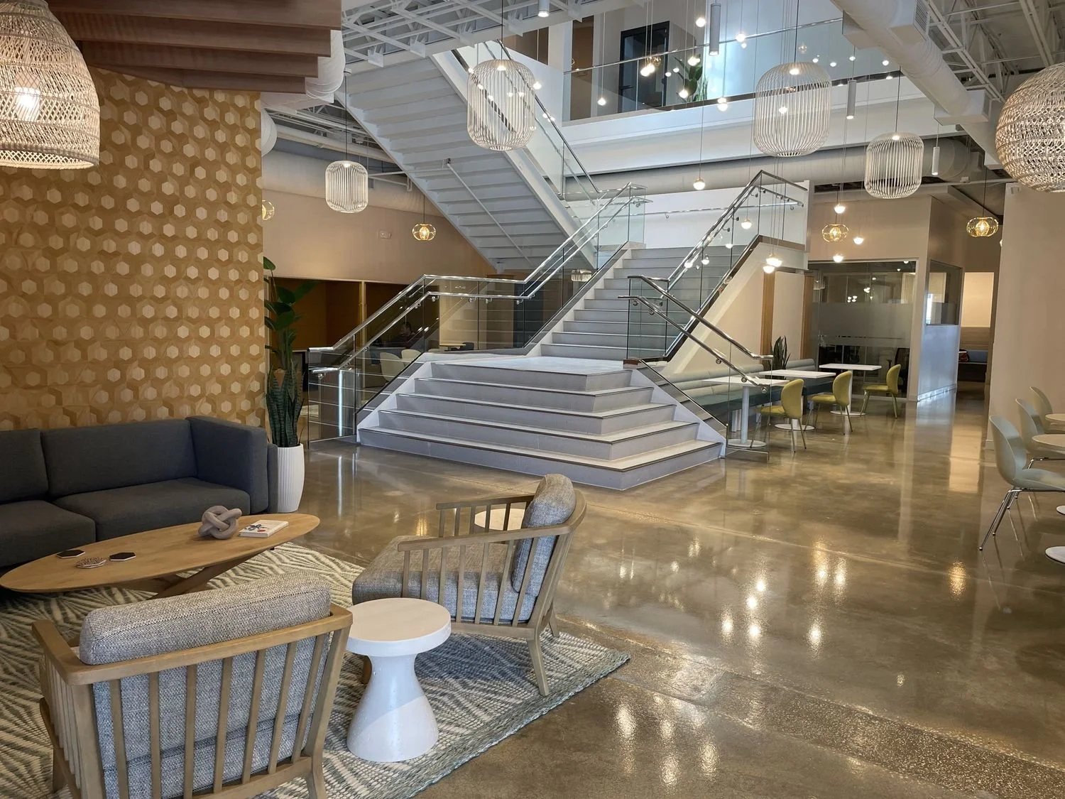 Modern lobby with a staircase, seating area, and decorative lighting fixtures.