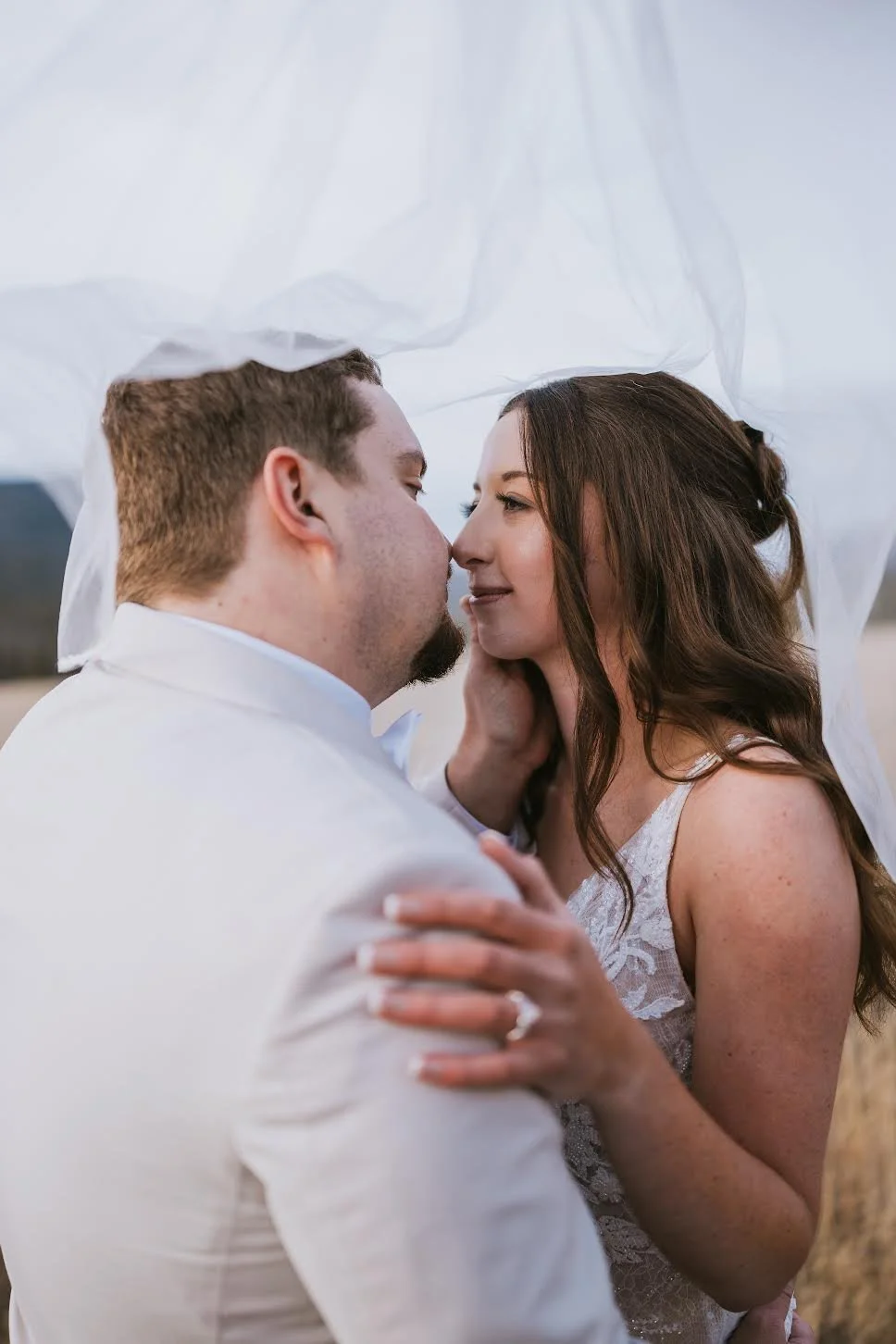 A couple dressed in white, about to kiss, outdoors with a light, airy background.