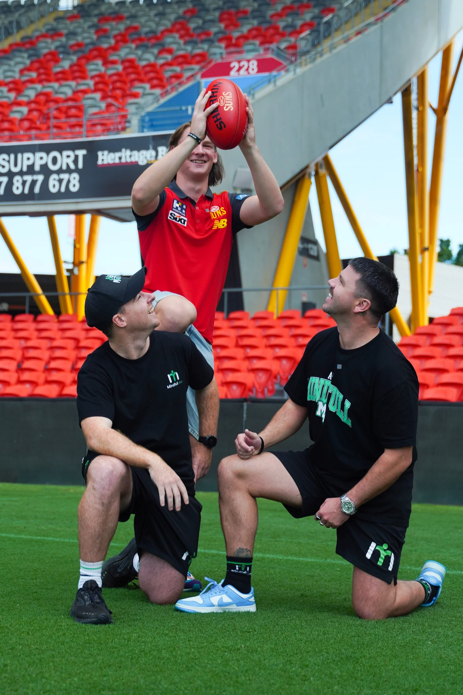 Three men on a football field celebrating with a red football