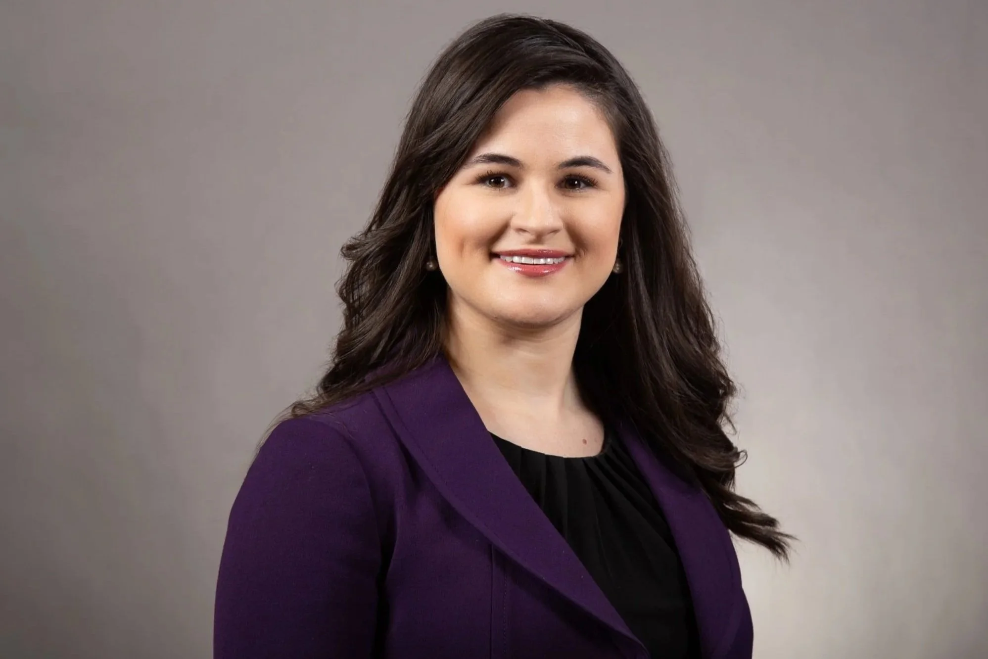 Portrait of a Vanessa Fox with long dark hair wearing a purple blazer and smiling against a plain gray background.