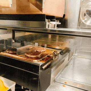 Beef Burger Patties are cooked on Alpha Grill and the built in spatula is automatically lifting and removing the cooked patties from the griddle to the warming tray without any human intervention.