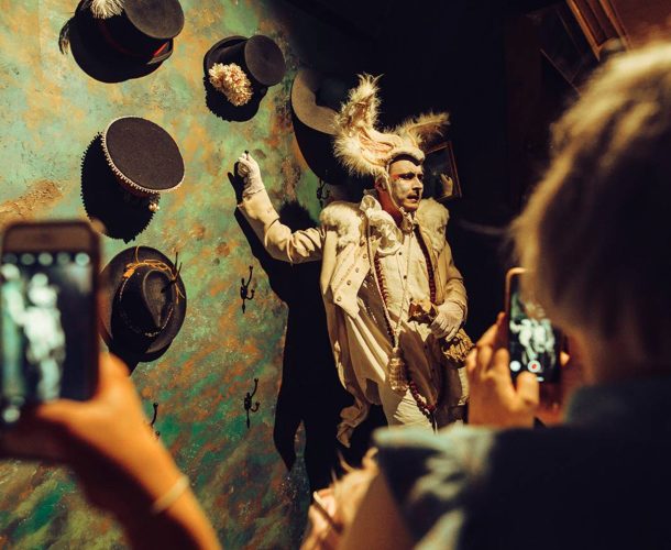 A Male performer, the audience are filing on their phones he is wearing a white rabbit costume.