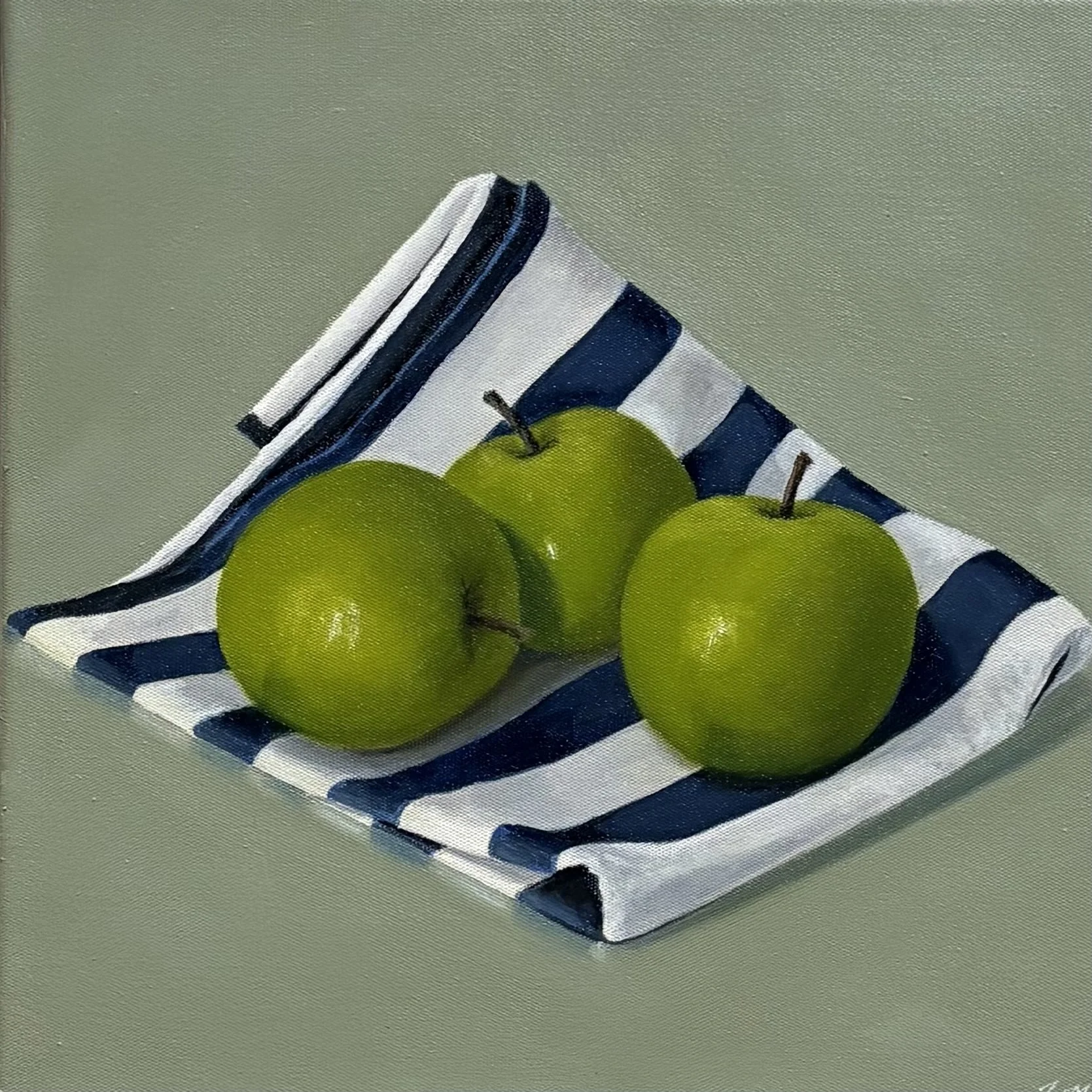 Three green apples placed on a cloth with blue and white stripes, on a gray surface.